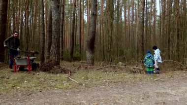 Çocuklar, sakin bir ormandaki bahçe işlerinde yetişkinlere yardım ediyor. Uzun ağaçlar ve doğa ile çevrili bir sonbahar gününün tadını çıkarıyorlar..
