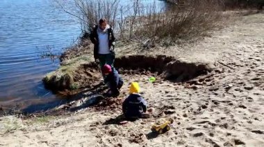 Çocuklar sakin bir gölün kenarında oynuyorlar, kumu kazıyorlar ve sıcak bahar güneşinin tadını çıkarırken yapılar inşa ediyorlar. Kahkaha ve sevinç bu huzurlu ortamda havayı dolduruyor..