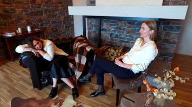 İki arkadaş rahat bir ortamda gevşek bir sohbete dalarlar, biri düşünceli bir şekilde otururken diğeri kanepeye yaslanır. Hava sıcak ve davetkar..