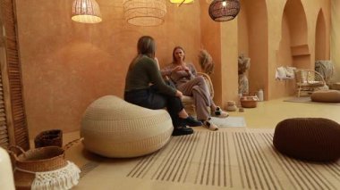Üç birey, doğal dokularla süslenmiş rahat bir alanda dostça bir sohbete girişiyor. Sıcak dekor, fikirleri paylaşmaya elverişli hoş bir atmosfer yaratıyor..