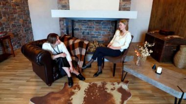 İki kadın sıcak bir oturma odasında rahatça oturup samimi bir sohbete dalıyorlar. Atmosfer doğal tonlar ve büyüleyici bir şömine ile bizi davet ediyor..