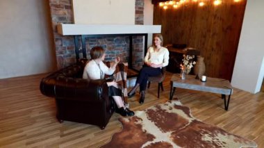 İki kadın, samimi bir oturma odasında kırsal bir şömine ve şık bir atmosfer içeren düşünceli bir sohbete girişiyor, kişisel bağlantı ve diyalogların altını çiziyor..