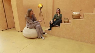 Rahatlatıcı ve iyi tasarlanmış bir mekanda, iki kadın derin bir sohbete dalarken, dünya renkleri ve dokularıyla çevrili yastıklı bir oturma seçeneğiyle rahatça otururlar..