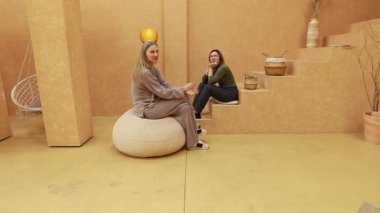 İki arkadaş sıcak dekore edilmiş bir mekanda rahat rahat oturup rahatça sohbet ediyorlar. Yumuşak ışıklandırma ve topraksı tonlar bağ kurmak için mükemmel bir atmosfer yaratır..