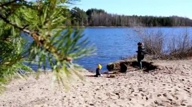 İki çocuk kumlu bir sahilde ağaçlarla çevrili sakin bir göl ve açık mavi bir gökyüzünün altında eğlenceli aktivitelere girişiyor. Huzurlu atmosfer keşif ve neşeyi davet eder..