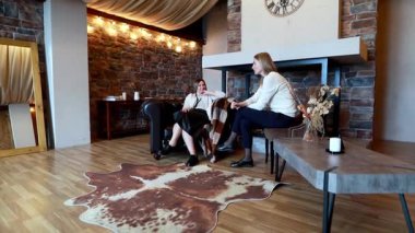 Kaba bir tasarıma sahip rahat bir oturma odasında, iki kadın rahat bir kanepede oturmuş, öğleden sonra birbirlerine eşlik ederek keyifli bir sohbete girişiyor..