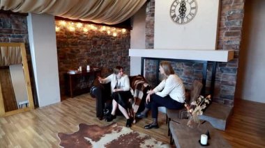 İki kadın sıcak bir şekilde aydınlatılmış, taşralı bir odada taş bir duvarla oturuyorlar. Etrafı rahat koltuklar ve yumuşak dekorasyon unsurlarıyla çevriliyken düşünceli bir konuşma yapıyorlar..