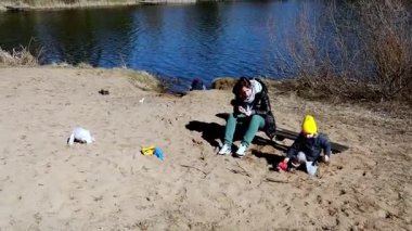 Bir anne, sıcak bir günde gölün kenarında çocuğunun kumlarda oynamasını izler. Diğer çocuklar yakınlarındaki çeşitli aktivitelerden zevk alırken doğa onları çevreleyip mükemmel bir rahatlatıcı atmosfer yaratıyor..