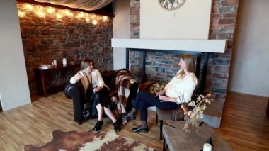 İki kadın sıcak ve davetkar bir salonda rahat bir kanepede oturur ve bitki ve hafif ışıklandırma gibi dekoratif elementlerle çevrili iken ilgi konularını tartışırlar..