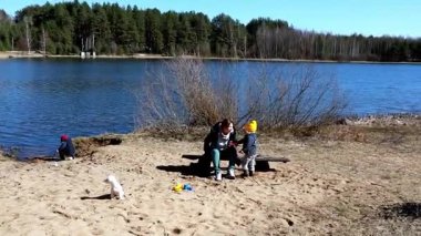 Göl kenarında açık, güneşli bir günde kumlu sahilde bir aile toplanır. Bir kadın yakınlarda otururken, iki çocuk oyuncaklarla oynuyor. Küçük bir köpek etrafı kolaçan ediyor..