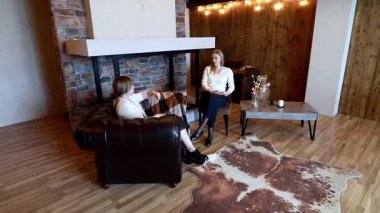 İki kadın şık ve sıcak bir mekanda kırsal bir şöminenin ve mobilyaların olduğu düşünceli bir tartışmaya giriyorlar. Atmosfer rahat ve dost canlısı..