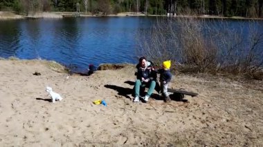 Bir aile güzel bir öğleden sonrayı göl kenarında köpeklerle oynayarak ve sıcak güneşin tadını çıkararak geçirir. Çocuklar eğlenirken gülerler..