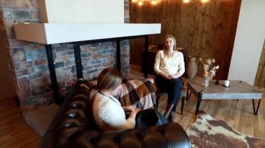 İki kadın, sıcak ve samimi bir tartışmanın tadını çıkarıyor. Sıcak, taştan bir şömine ve ahşap aksanlı bir mekanda. Kış boyunca rahat bir bağ ortamı yaratıyor..