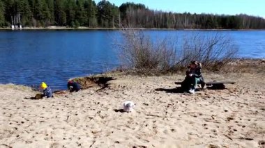 Bir yetişkin yakınlarda dinlenirken çocuklar gölün yanındaki kumda oynuyorlar. Güneşli bir gün ve manzaralı bir zemin su kenarında mükemmel bir aile atmosferi yaratır..