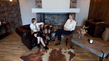 İki arkadaş, sıcak ve davetkar bir oturma odasında rahat bir oturma alanı, kırsal bir dekor ve rahat bir ortam içeren rahat bir sohbetin tadını çıkarıyorlar..