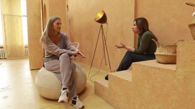 İki kadın, şık ve sıcak renklerle dolu bir odada oturup sohbet ederler. Fasulye torbası ve merdivenlerde otururken hareketli bir sohbete dalarlar ve davetkar bir atmosfer yaratırlar..