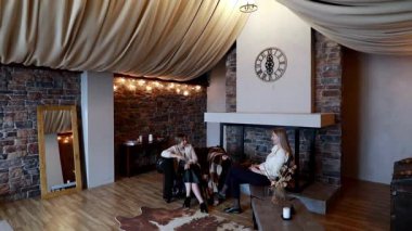 İki kadın, yumuşak bir yüzeyde, davetkar ve şık bir odada derin bir sohbete dalarken rahat bir şekilde otururlar. Sıcak ışıklandırma ve dekor hoş bir atmosfer yaratıyor..