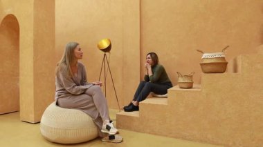 İki kadın sıcak tonlarda ve kendine özgü dekorlarla dolu rahat, sanatsal bir mekanda oturuyor. Özenle hazırlanmış mobilyalar ve el yapımı eşyalarla çevrili düşünceli bir tartışmaya girişirler..