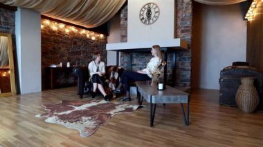 İki kadın sıcacık bir köy odasında rahat bir şekilde oturup hoş, taştan bir şöminenin yanında düşünceli bir sohbet ediyorlar. Atmosfer davetkar ve rahatlatıcı..