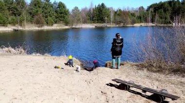 Bir yetişkin onları izlerken çocuklar gölün yanında yaratıcı oyunlardan hoşlanırlar. Berrak mavi su, ilkbaharın başlarında yemyeşil ile çevrili parlak gökyüzünü yansıtır..