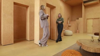 İki kadın, minimalist bir stüdyoda, sıcak toprak tonlarının ve doğal dokuların yer aldığı düşünceli bir sohbete girişiyor. Uzay sakin ve davetkar bir atmosfer yaratır..