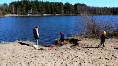 Bir kadın onları izlerken çocuklar gölün kenarında oynamaktan zevk alır. Açık bir günde güneş ışıl ışıl parlıyor. Açık havada eğlence ve doğa keşfi için mükemmel bir zemin sunuyor..