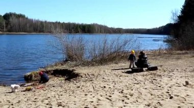 Çocuklar göl kenarında güneşli bir günün tadını çıkarırlar, kumda oynarlar ve bir köpek onlara eşlik ederken keşfe çıkarlar. Berrak manzarayı çevreleyen yemyeşil ağaçlar barışçıl bir atmosfer yaratıyor..