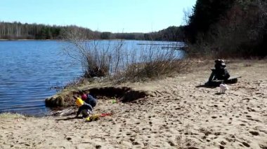 Çocuklar manzaralı gölün kenarlarında oyun oynamaktan ve inşa etmekten hoşlanırlar. Bir yetişkin, sıcak bir günde, güzel açık havada, kumların üzerinde huzur içinde oturur..