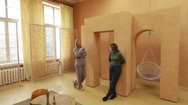 İki kadın, eşsiz bir dekorasyon ve rahat bir koltuğun bulunduğu sıcak, davetkar bir odada hafif bir sohbete girişiyor. Atmosfer gevşemeyi ve bağlanmayı teşvik eder..