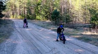 İki arkadaş kumlu orman yolunda bisiklet sürmekten hoşlanıyor. Biri bisikletini iterken diğeri öne geçiyor. Berrak gökyüzü ve yemyeşil alan onların günü için mükemmel bir zemin oluşturur..