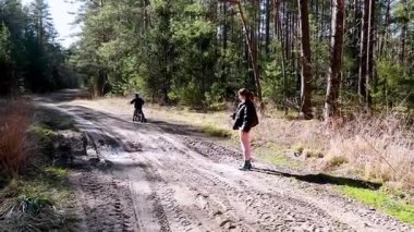 Bir çocuk kumlu bir orman patikasında bisiklet sürerken, bir yetişkinin dışarıda durup, huzurlu bir doğal ortamın tadını çıkarırken bahar mevsimi ılık getirir..