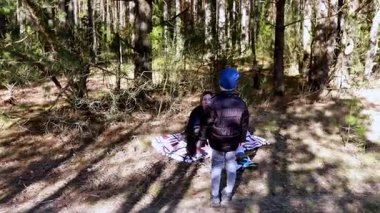 Bir çocuk, ağaçlarla çevrili sakin bir ormanda duruyor. Sahne, doğanın sessiz keşfini yakındaki oturulacak rahat bir battaniyeyle yakalar..