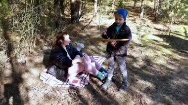Oğlu yakınlarda dururken bir anne ormanda bir battaniyeye oturur. Ağaçlar ve güneş ışığıyla çevrili olarak yiyeceklerini paylaşıyorlar ve birlikte huzurlu zamanlarının tadını çıkarıyorlar..