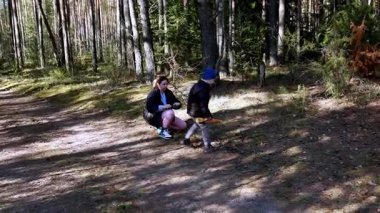 İki çocuk uzun ağaçlarla çevrili bir orman patikasında geziniyor. Kahkaha ve keşiflerle dolu güneşli bir günün tadını çıkarıyorlar..