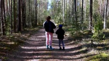 Bir kadın ve bir çocuk, uzun ağaçlar ve benekli güneş ışığıyla çevrili, huzurlu bir orman yolunda yürürler. Doğanın sakinliği keşif ve bağlanma için mükemmel bir kaçış sunar..