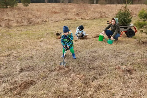 Güneşli bir günde, iki çocuk ve bir yetişkin çimen tarlasında birlikte çalışırlar. Çukur kazıyorlar ve taze ağaçlar dikiyorlar. Temiz havanın ve doğanın tadını çıkarıyorlar..