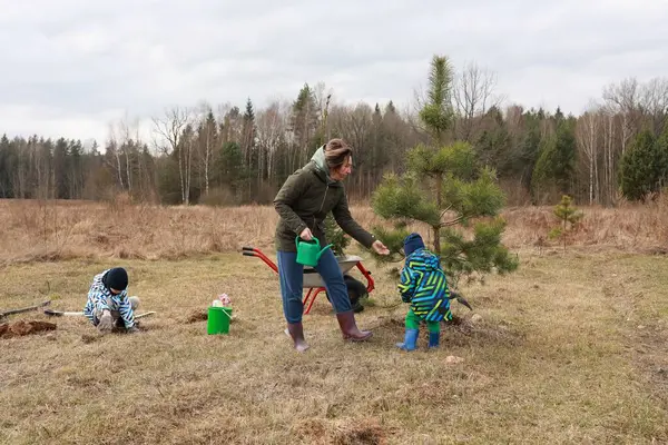 Bir kadın ormanın yakınındaki bir tarlada iki çocuğun genç ağaçlara bakmasına yardım eder. Bir çocuk bitki yetiştirirken, diğeri bir ağacı sularken, doğada takım çalışması sergiliyor..