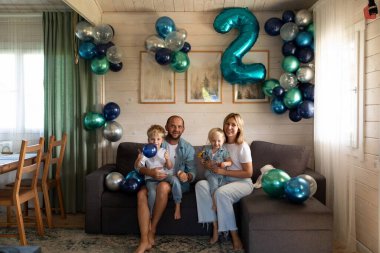 Bir aile, renkli balonlar ve neşeli bir atmosferle ikinci yaş gününü kutlamak için evde doğum günü partisinin tadını çıkarır. Oturma odası sıcacık dekore edilmiş..