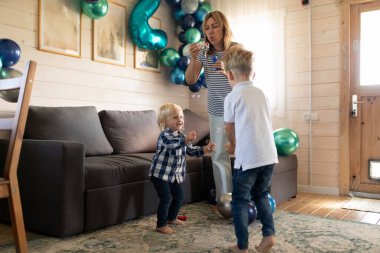 İki genç çocuk balonlarla dolu parlak bir oturma odasında neşeyle kabarcıklarla oynuyorlar. Onlar hevesle onları kovalarken anneleri baloncukları üflüyor, eğlenceli bir atmosfer yaratıyorlar..