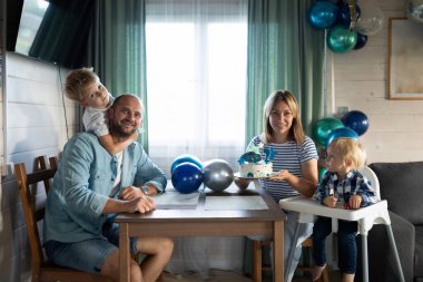 Bir aile sıcak bir odada ikinci yaş gününü kutluyor. Neşeli ortam balonları, mumlu pastayı ve neşeli ifadeleri içeriyor. Birlikte geçirdiğimiz özel bir anı vurguluyorlar..