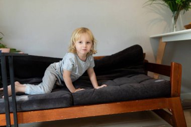 Genç bir çocuk, aydınlık bir oturma odasındaki yumuşak, siyah bir yatakta mutlu bir şekilde emekliyor. Atmosfer neşeli ve davetkar, bitkiler doğaya bir dokunuş ekliyor..