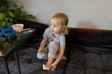 Genç bir çocuk, aydınlık bir odadaki rahat bir kanepede rahatça oturur. Çocuk atıştırmalıkları renkli çatal bıçaklar ve yakında bulunan bitkilerle çevrili..