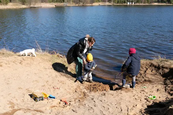 İki genç çocuk sakin bir gölün yakınında kumlarla oynaşırken bir yetişkin onları denetliyor. Sahne güneşli bir bahar gününde açık gökyüzüyle çekilmiştir..
