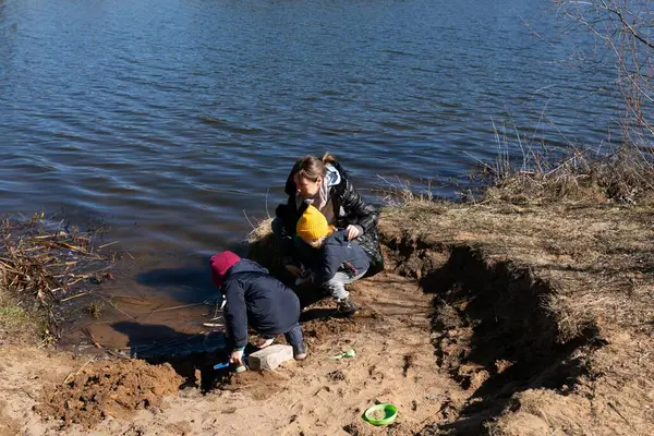 Baharın başlarında güneşli bir günde, iki çocuk bir yetişkin gözlemlerken kumlu nehir kıyısını keşfeder. Bölge su ve otlarla çevrili. Macera ve oyun anlayışı gelişiyor..