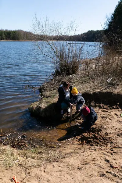 Üç çocuk neşeyle bir nehir kenarında oynuyorlar, kumu kazıyorlar ve sığ suları keşfediyorlar. Güneşli gün, doğal çevrenin güzelliğini arttırır..