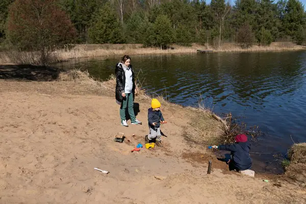 Bir anne göl kenarında oynayan iki çocuğunu gözlemler. Bir çocuk kumlara inşa ederken diğeri sığ sulara sıçrarken güneşli bir bahar gününün tadını çıkarıyor..