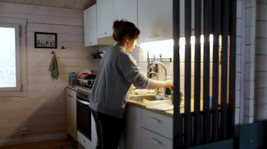 Bir kadın sıcak bir mutfakta sebze doğramakla ve tabak düzenlemekle meşgulken, yumuşak ışıklandırma mekanı aydınlatıyor. Akşam sükuneti rahatlatıcı bir atmosfer yaratır..