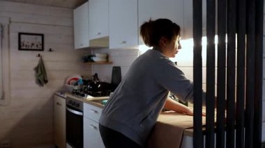 Bir kadın mutfağı temizler, bulaşıkları kurutur ve onları uygun yerlerine yerleştirir. Yumuşak ışık, bu davet edilen ev ortamında sıcak bir atmosfer yaratır..