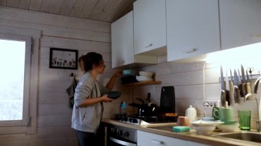 Sıcak bir ahşap mutfakta, bir kadın ustalıkla besleyici bir yemek hazırlar. Bulaşıkları yerleştirirken güneş ışığı pencereden akar ve rahat bir atmosfer yaratır..