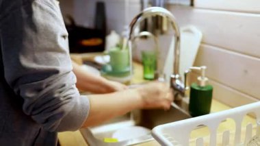 Bir insan, doğal ışıkla dolu sıcak bir mutfak ortamında bulaşıkları yıkar. Mutfak aletleri lavaboda temizleniyor, sakin ve düzenli bir atmosfer yaratıyorlar..